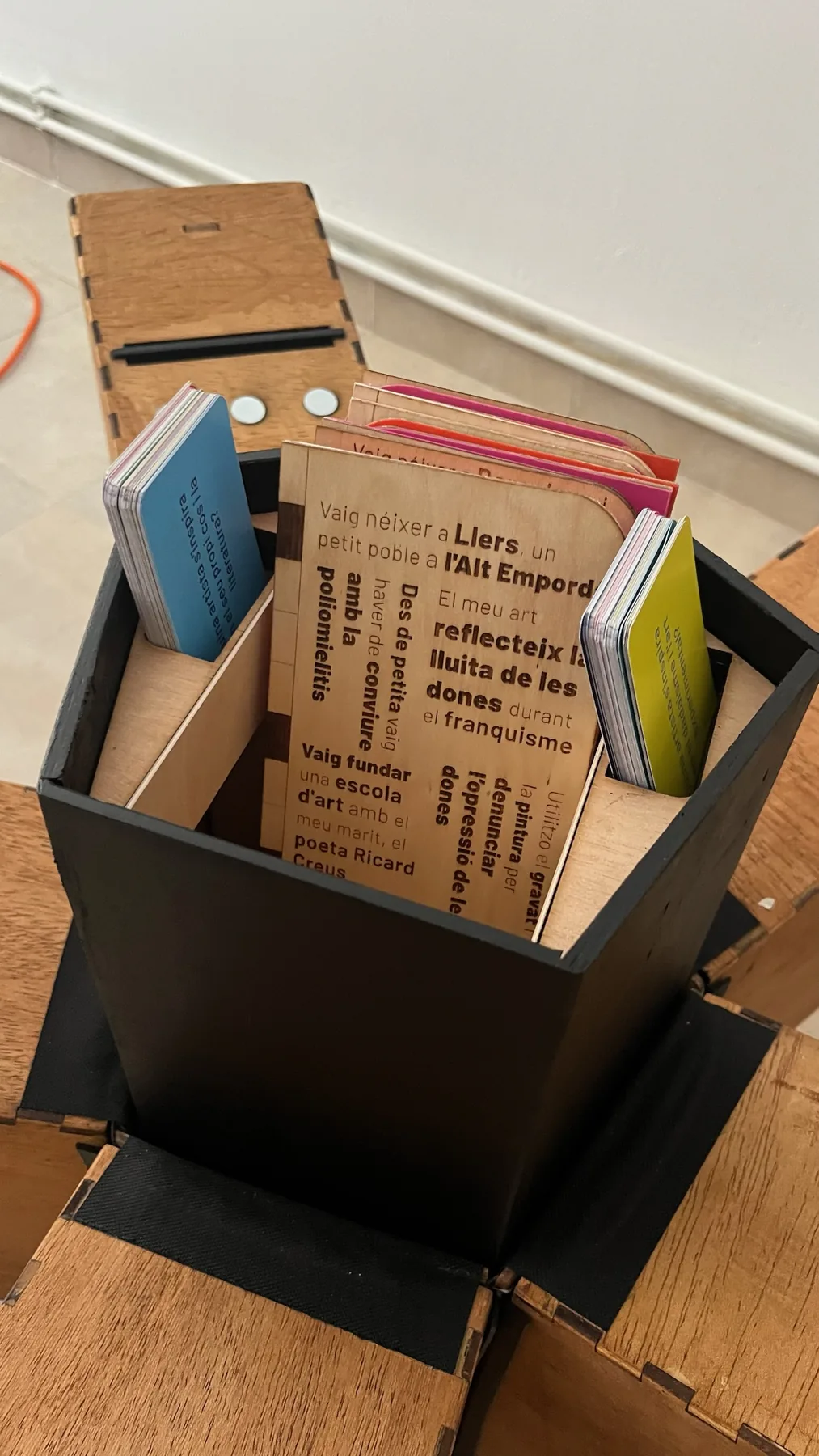 Conjunto de tarjetas biográficas de Pioneres dentro de una caja de madera.