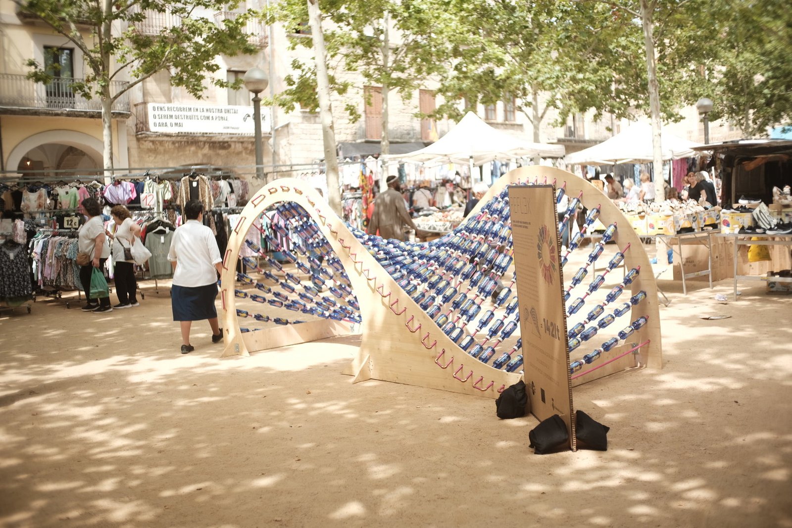 Instalación REFLEX desplegada en una plaza, formada por una estructura ondulada con botellas reutilizadas.